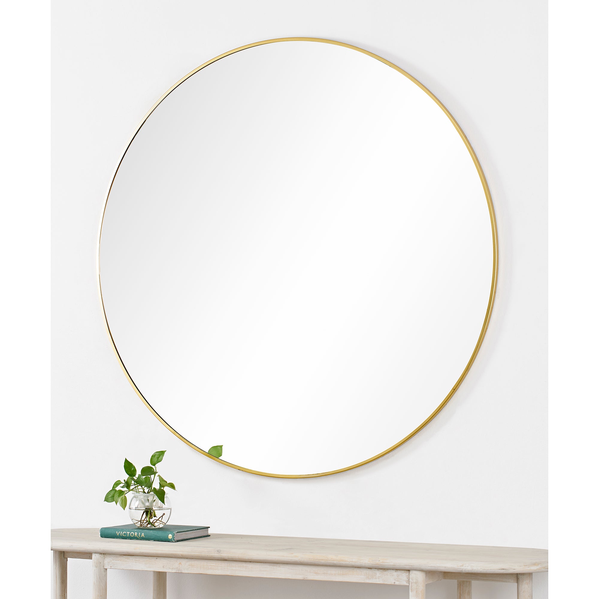 Fragoso Wall Mirror mounted on a wall above a table with a plant and book, displaying elegance.