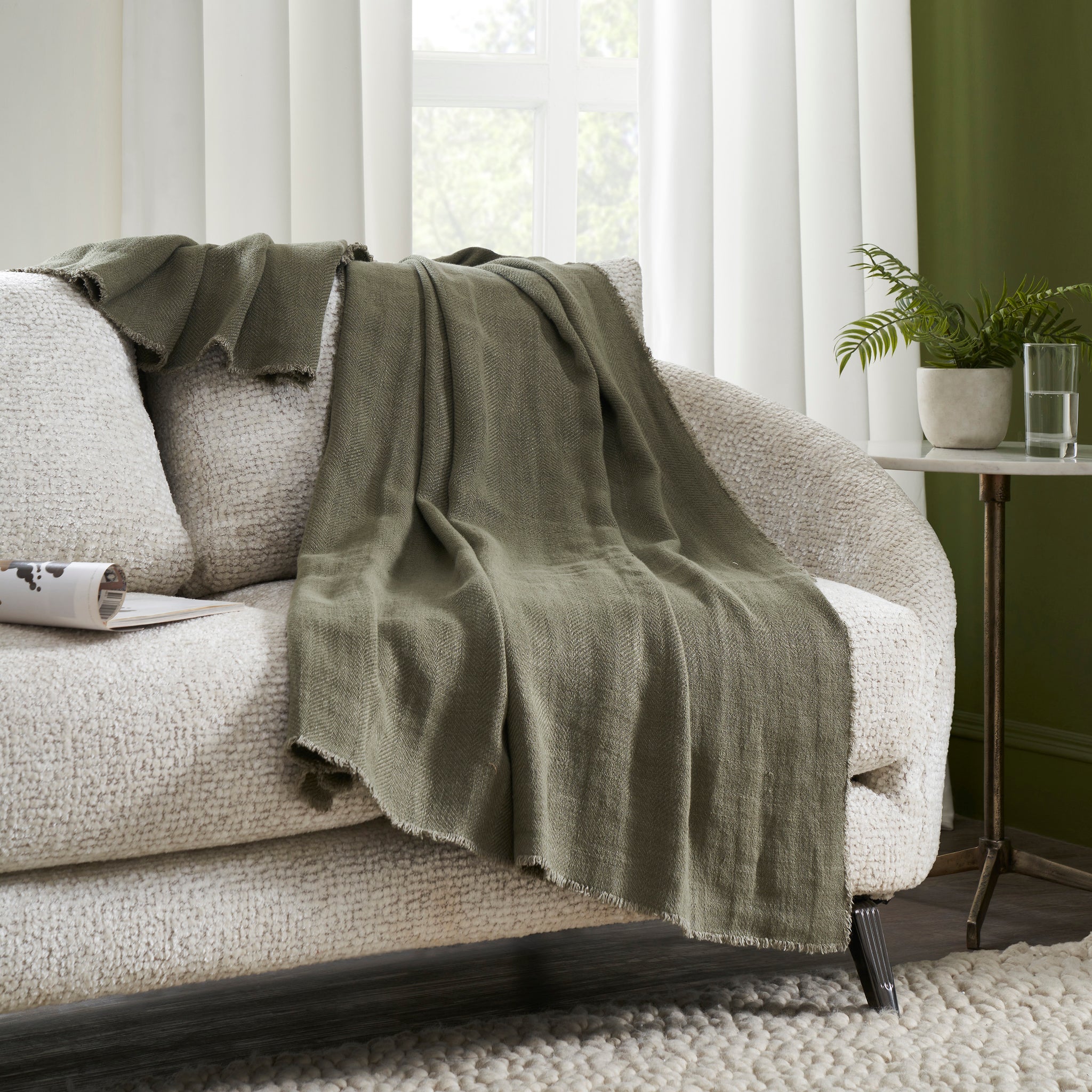 Vernier Throw in olive green, elegantly draped over a textured cream sofa in a bright room.
