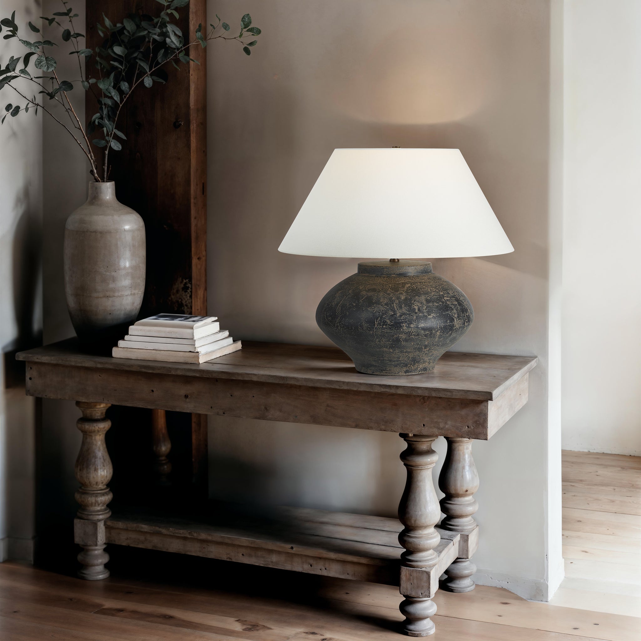 Patina table lamp beside a vase and stacked books on a rustic wooden table