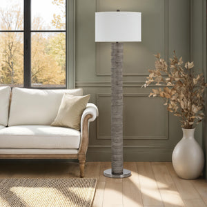 Moringa floor lamp in a living room setting beside a white sofa and decorative plant.