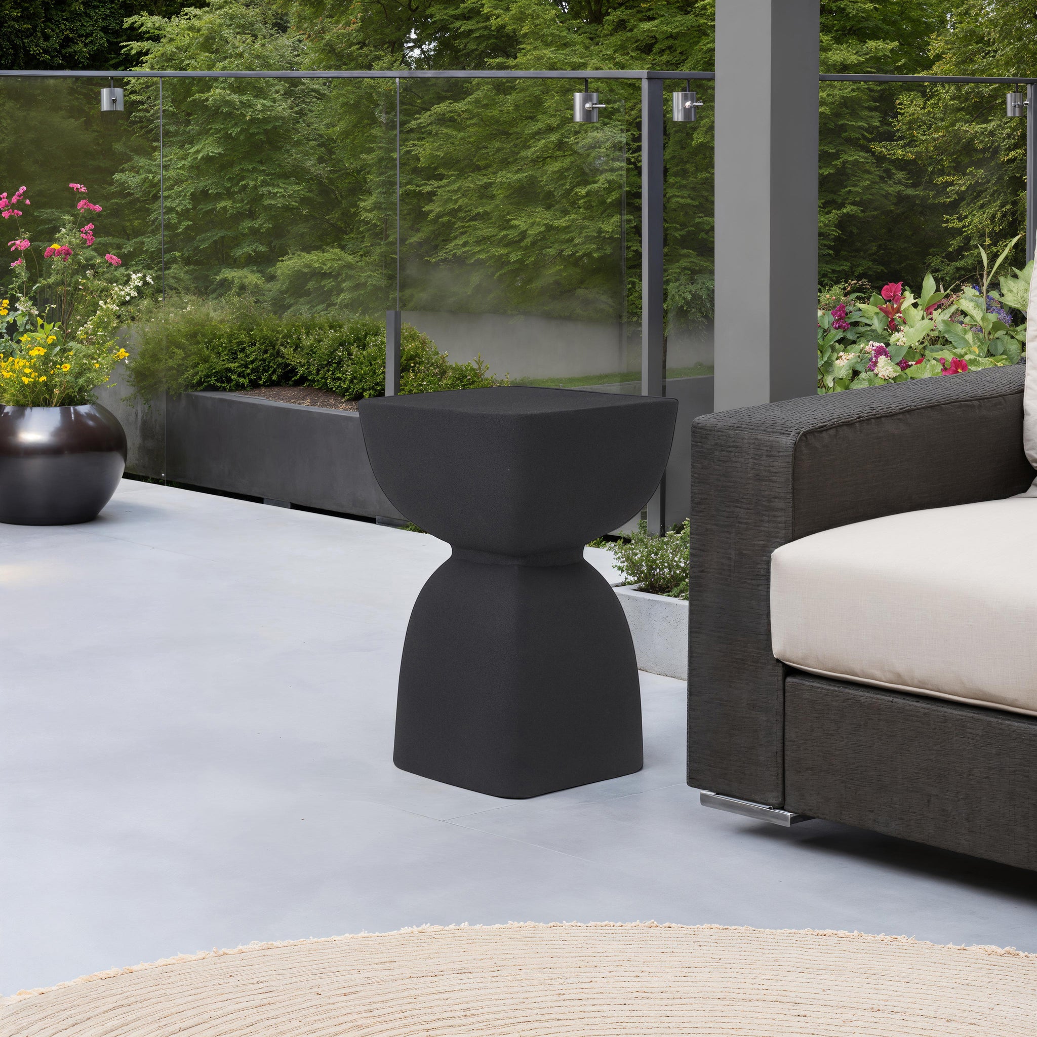 Frans Outdoor Side Table in black on a patio, next to a sofa and plants.