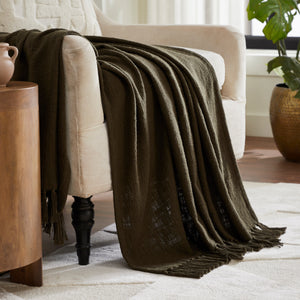 Chalamet Throw Blanket draped over a beige armchair, showcasing its dark green color.