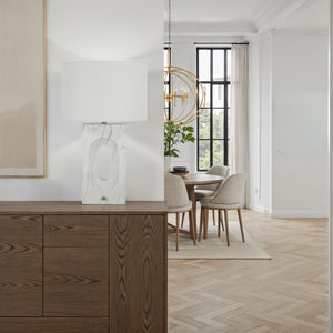 Scriba table lamp on a wooden sideboard in a bright living space with dining area.