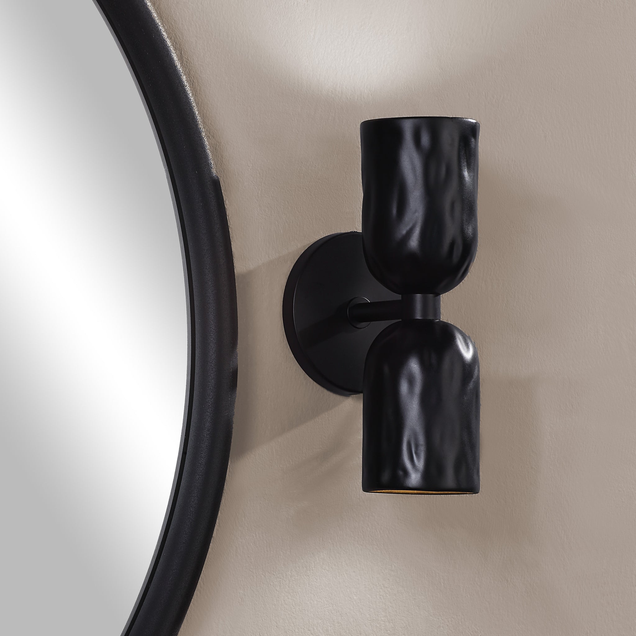 Alessia wall sconce in black mounted beside a round mirror, emphasizing its modern design.