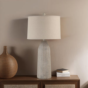Lechuga Table Lamp on a wooden side table, with a beige shade and textured gray base, styled with decor.