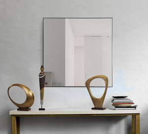 Greer mirror by Renwil displayed above a console table with decorative sculptures and books.