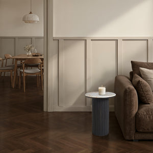 Alessio accent table with a candle next to a brown sofa in a cozy living space.