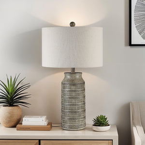 Tarragona Table Lamp on a nightstand with plants and books, showcasing its gray ceramic base and beige shade.