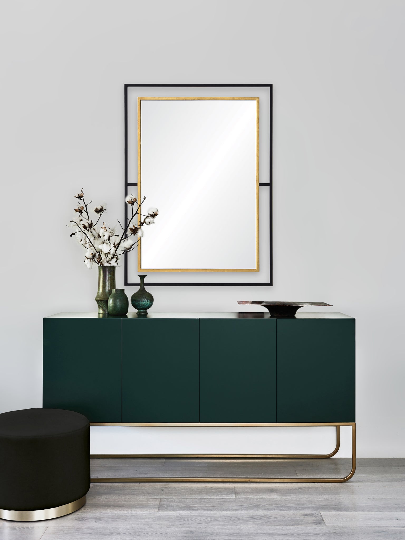 Gray wall mirror above a green cabinet, styled with decorative vases and a black stool.