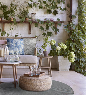 Skye pillow in blue placed on a cozy outdoor seating area with greenery.