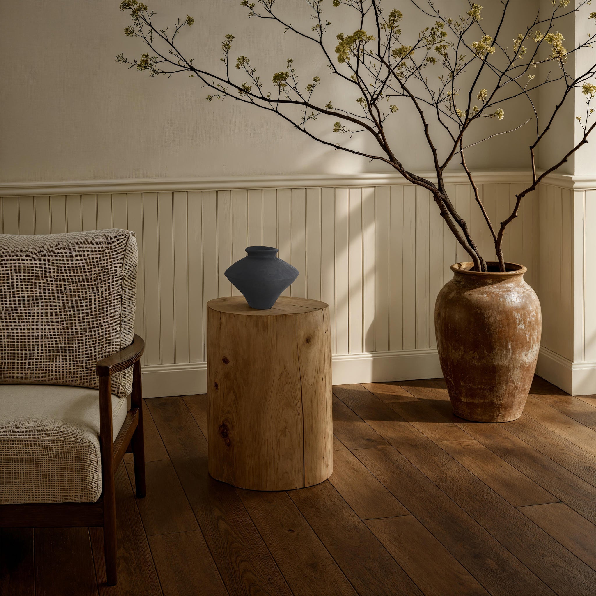 Mills vase by Renwil on a wooden stool beside a chair and a large ceramic pot