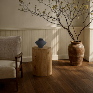 Mills vase by Renwil on a wooden stool beside a chair and a large ceramic pot