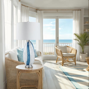 Solis Table Lamp in a bright living room setting with ocean view, white shade, and blue glass base.